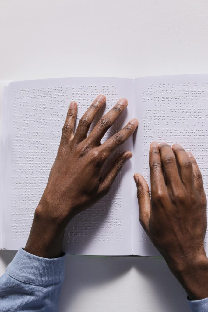 Hands gently reading a Braille book, symbolizing accessibility and education.